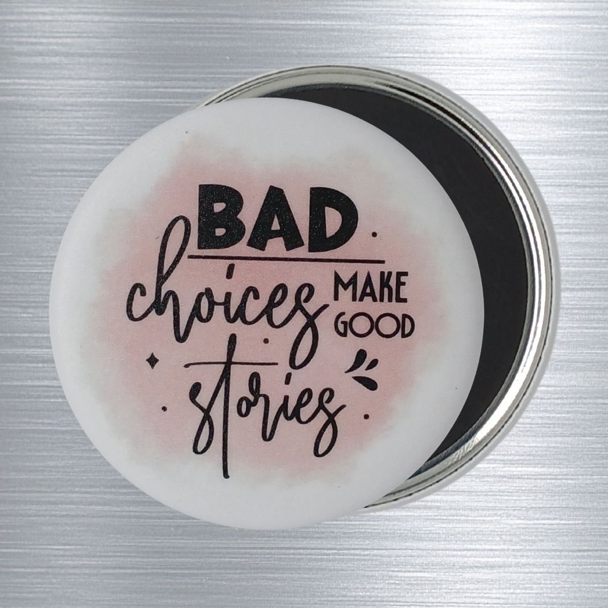 A white, round fridge magnets with a pink splash of color. The funny text design is in black and reads "Bad choices make good stories.