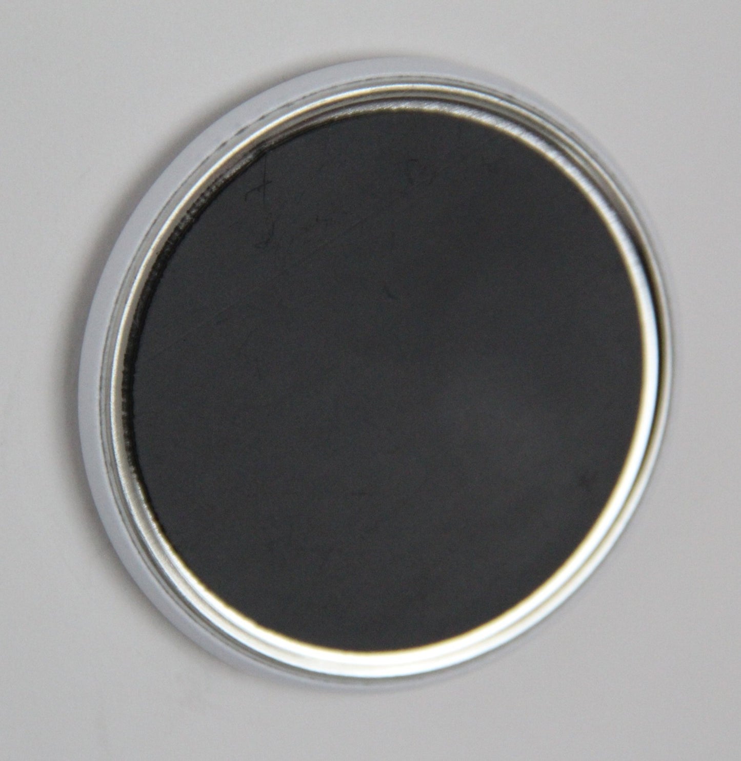 Back of a round, white refrigerator magnet. The black magnet covers almost the whole backside.