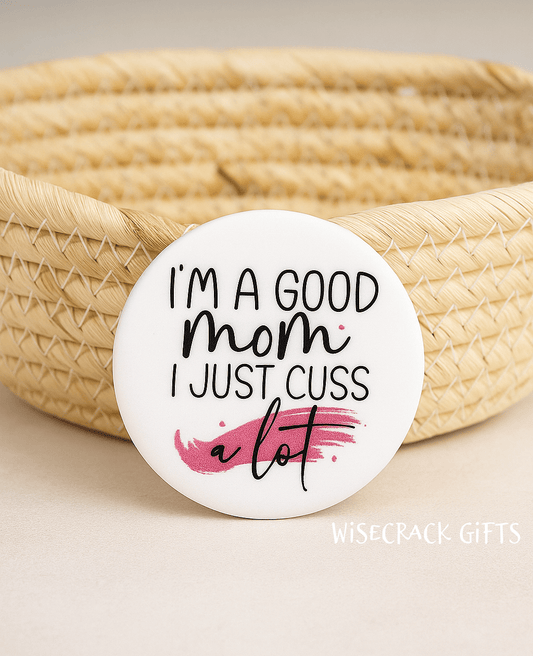 White button that reads I'm a good mom I just cuss a lot. Wisecrack Gifts is the creator with the name in the bottom corner.